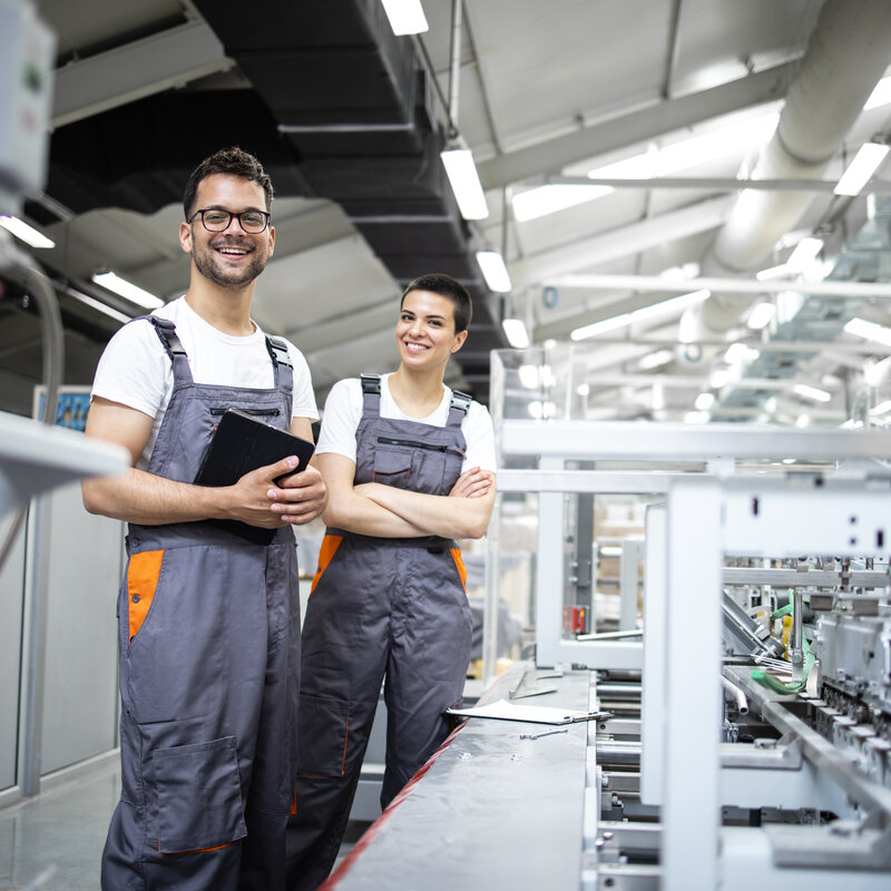 Porträt von Produktionslinienarbeitern, die den Herstellungsprozess einer modernen Verpackungsindustriemaschine in der Druckerei steuern.